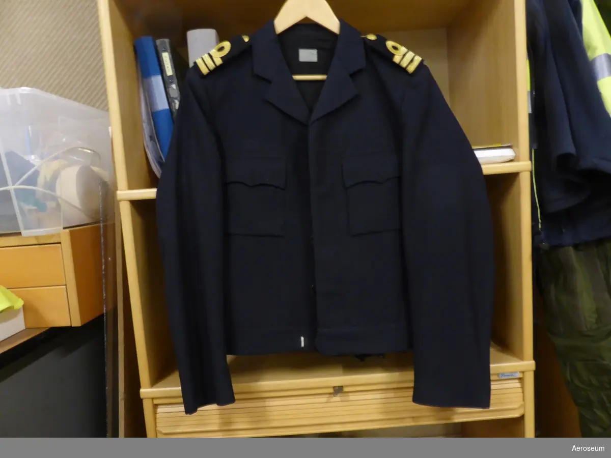 Två kolli med uniformsrock, byxor, och midjejacka. Tillhörigt "Stor-ben". Kläderna är mörkblåa med guldfärgade detaljer. Midjejackan är storlek C48, den mörkare byxan med kraftigare tyg har storlek C48, medan den andra byxan har storlek 50C.