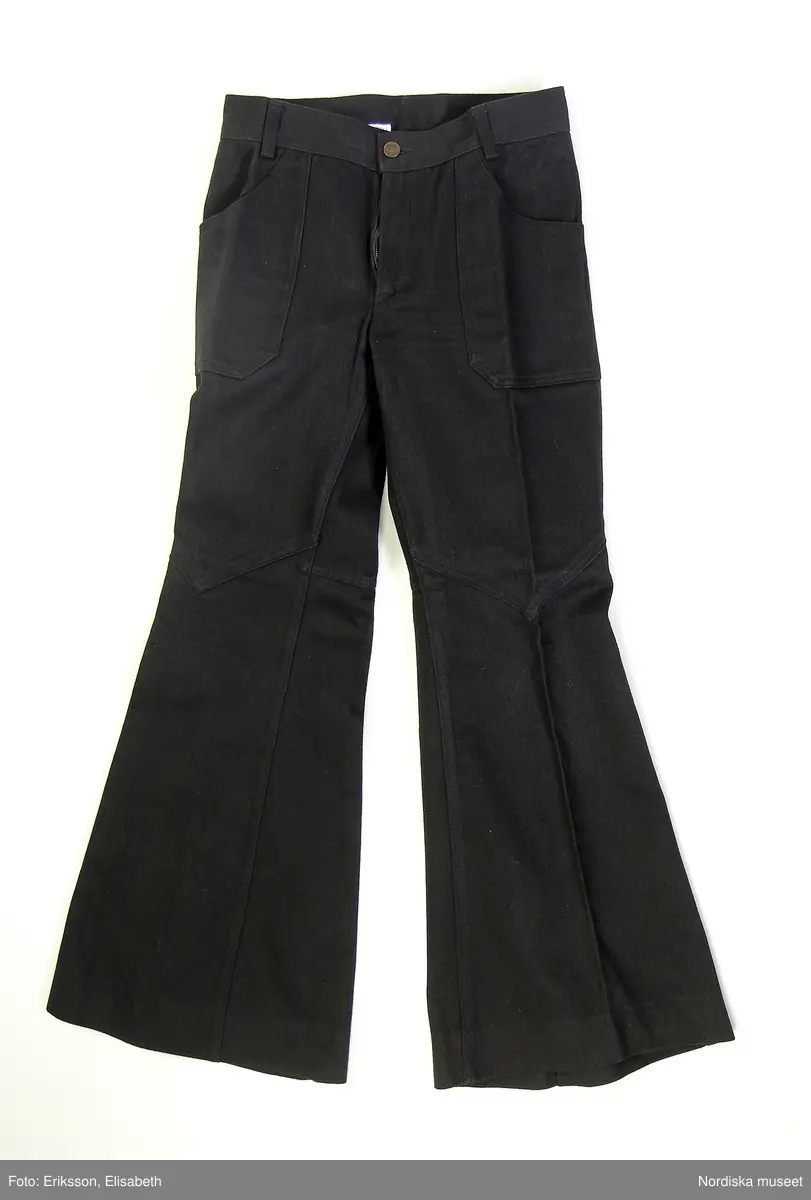 Byxor från Gul & Blå i svart jeans med medelhög midja och svarta sömmar. Storlek 44, herrstorlek.
Jeans helt utan slitningar. 
4 framstycken och 4 bakstycken. Utsvängda nedtill och åtsittande upptill. Besparing bak på jeansen. Fåll i nederkant 5 cm.
Snittet fram på knät är format som ett V, som delar övre benstycke med det nedre. Pressveck fram och bak på vardera ben.
Två större utanpåliggande kantiga fickor fram, gylf med blixtlås av plast och patentknapp i metall med stansat ”Gul & Blå”. 2 fickor bak. 
/Hanna Leijon 2019-03-13