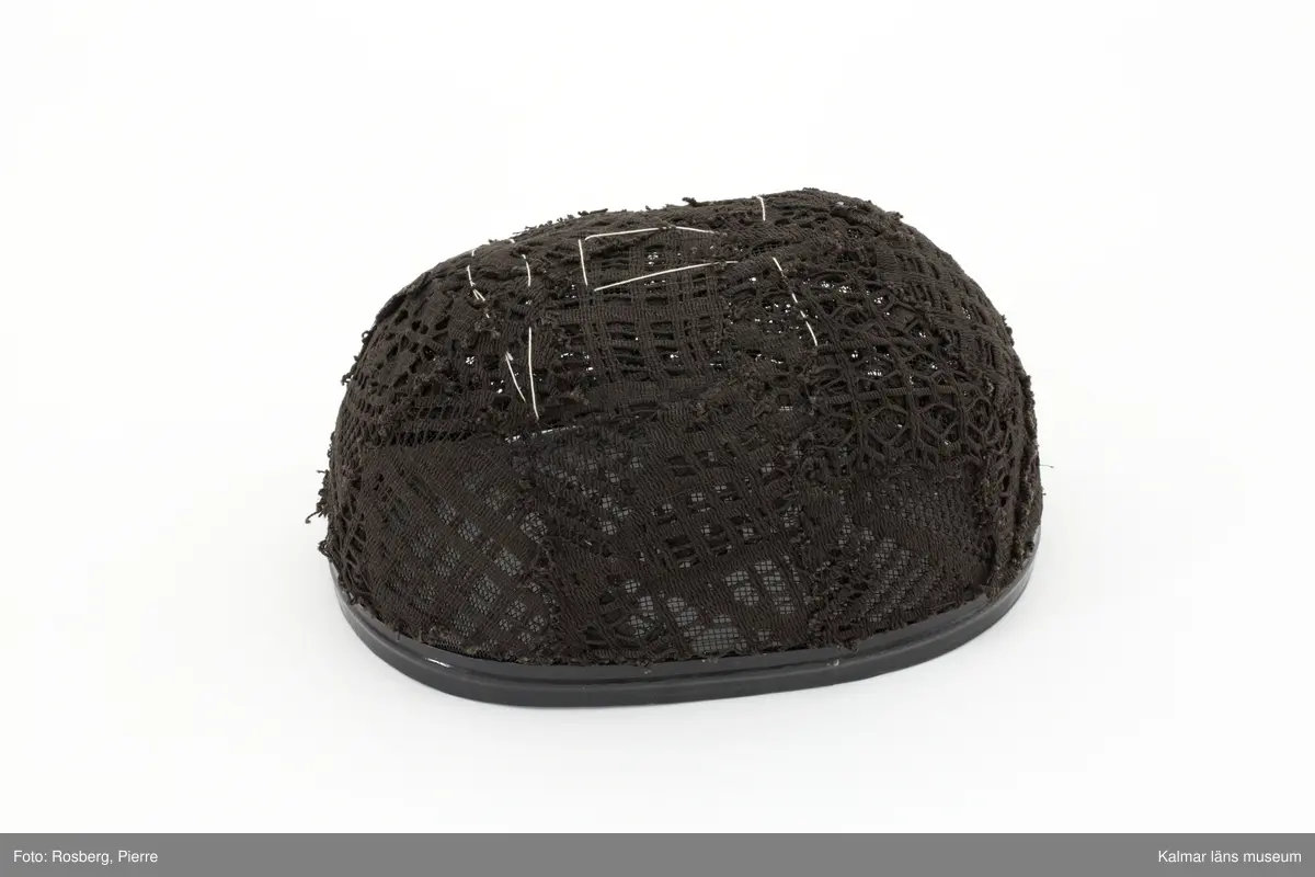 Svart oval fäktarmask med broderade ansiktsdrag i vitt.