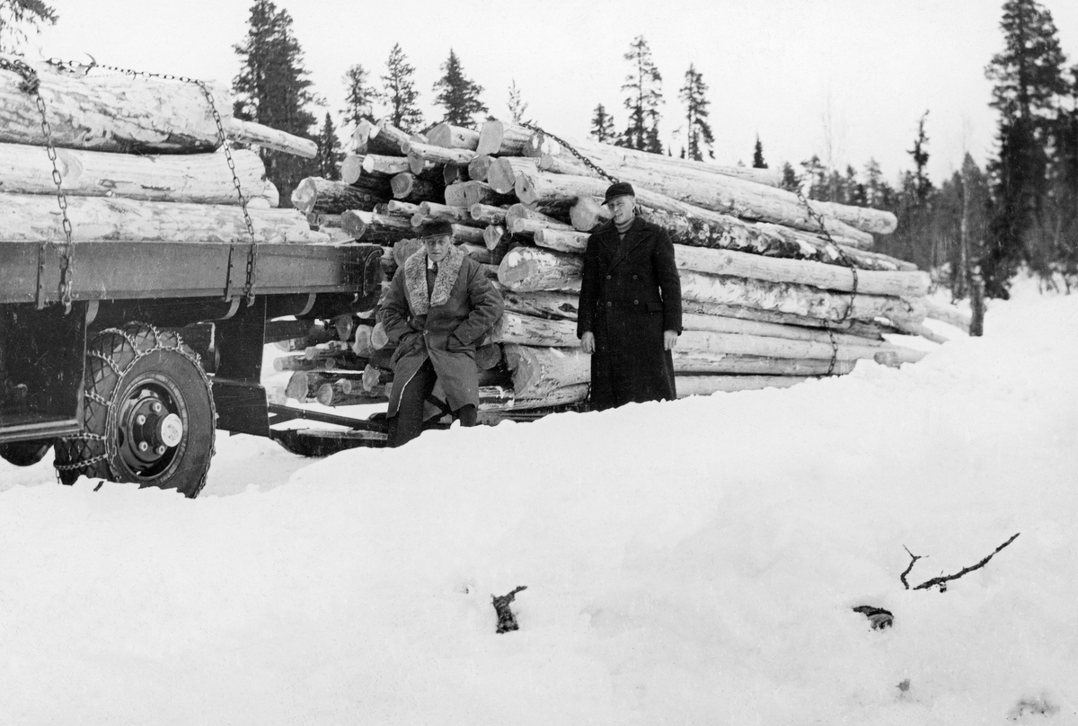 Tømmerkjøring med lastebil i Femundstraktene 1936.  Vi ser bakparten på lastebilen, som har en del tømmer som er fastspent med kjettinger, på planet.  Bilen har kjettinger også på bakhjulene.  Bak bilen er det montert en slede med et for sin tid enormt tømmerlass, også dette festet med kjettinger. Transporten skal ha omfattet 15 kubikkemeter tømmer (fastmål).  I forkant av sleden sitter/står to karer i vinterfrakker.  Jfr. DSS 3149. Bilen tilhørte Kåre Fredheim (1909-1987) på Drevsjø.