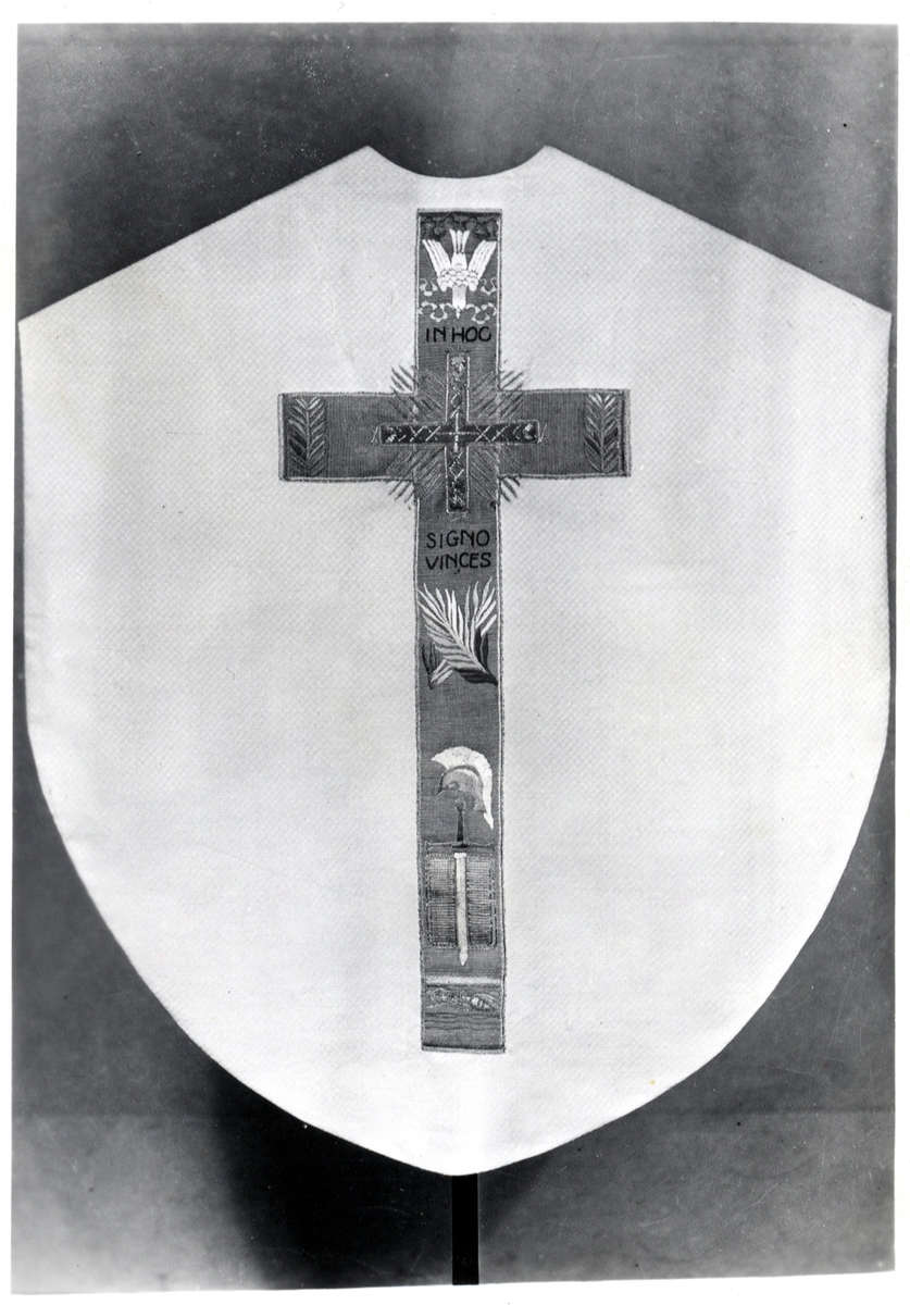 Foto (svart/vitt) av en ljus mässhake (framsidan) med mörkare broderat parti, med diverse kristna symboler och text: "In Hoc Signo Vinces". 

Inskrivet i huvudbok 1983.