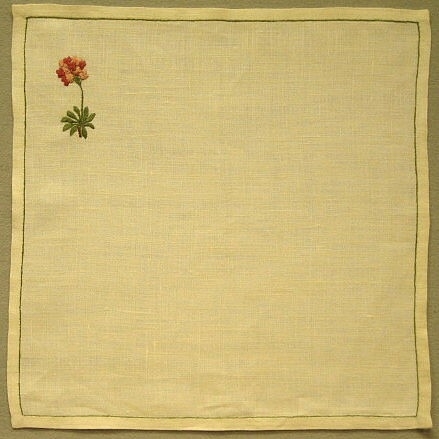 Halvblekt tablett i linne med broderad blomma i grönt och rosa. Blomman är broderad i plattsöm och stjälksöm och placerad i övre vänstra hörnet.Denna modell samt inv.nr. 1105-1113, 1115-1116 komponerades under 1980-talet, då det gick trögt för Hemslöjden. Tabletterna var tänkta att säljas styckvis.Skiss, se inv.nr. 1120:32.