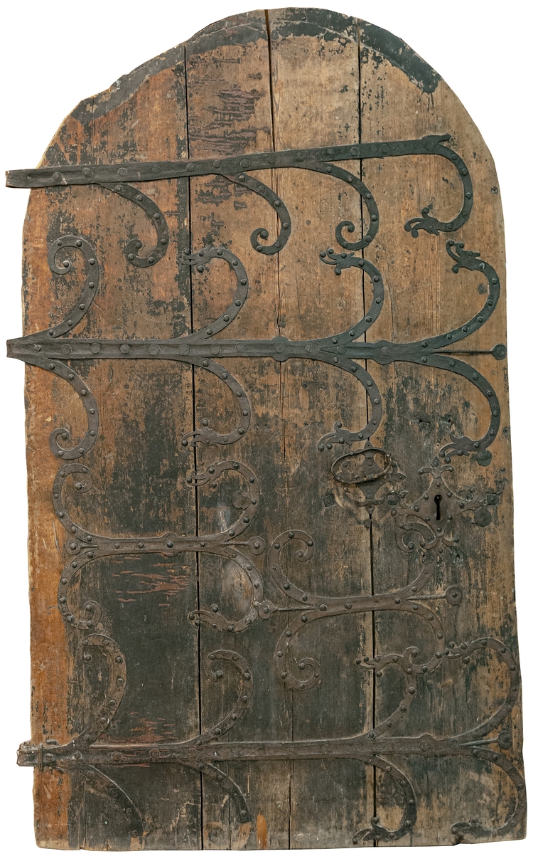 Kyrkdörr, romansk, kyrkport, med järnornament och beslag. Dörren består av tre lodräta, tjocka furuplankor, rundad upptill. Tre kraftiga gångjärn. I övrigt rikligt järnbeslagen. I ändarna av beslagen på en del ställen gapande djurhuvuden. Spår av tjära. Flera ristningar, bland annat armborst, konsekrationskors (invigningskors).