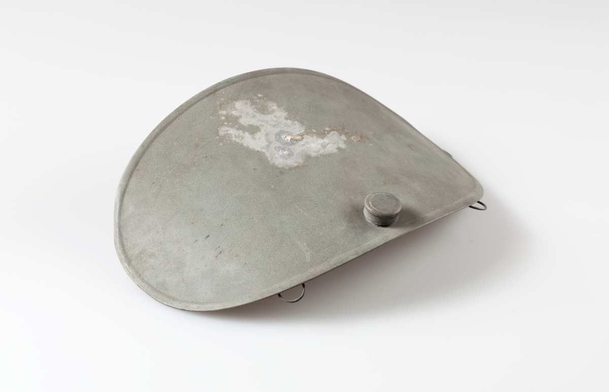Oval, buet varmeflaske i sink med skrukork. Metallhemper langs øvre kant.