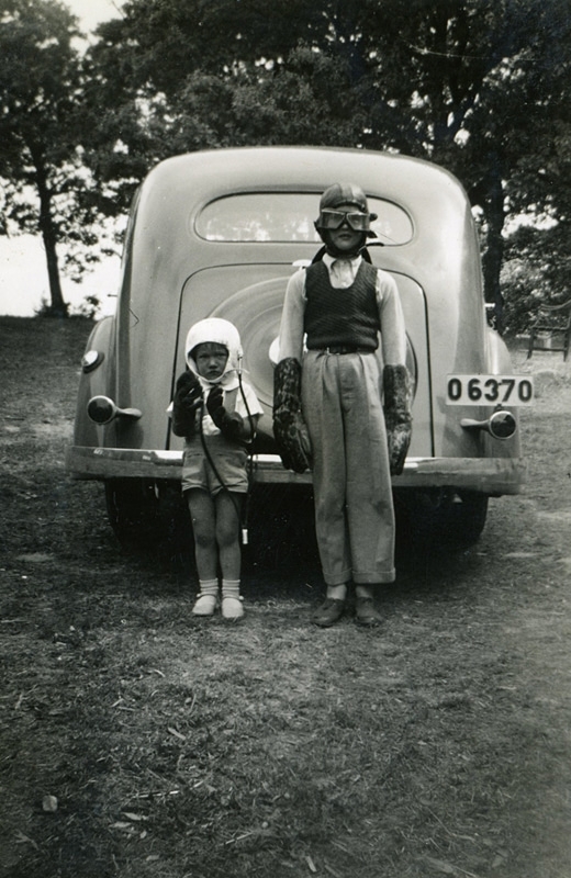 Två böder står uppställda framför en Volvo PV51-52 årsmodell 1937, Sporred Tvärgården 1930-tal. Från vänster: Fredrik och Magnus Lagerman. Fredrik har på sig en skinnhjälm samt ett par skyddsglasögon. Detta var en vanlig utstyrsel vid bilfärd. Deras föräldrar ägde Sporred Tvärgård.