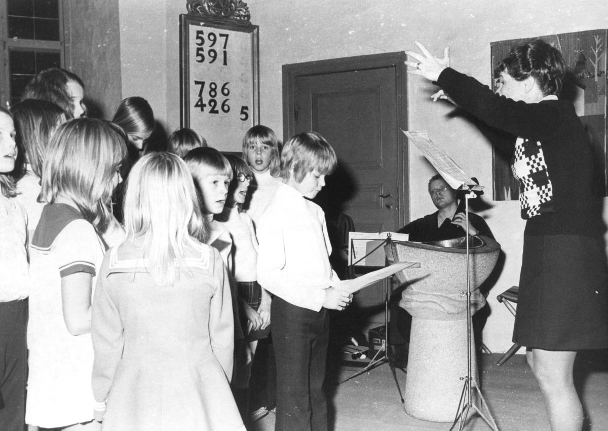 Kållereds kyrka (Svenska kyrkan) cirka 1970.
Till höger: körledare/organist Eva Karlsson, Kållered, leder barn som sjunger.