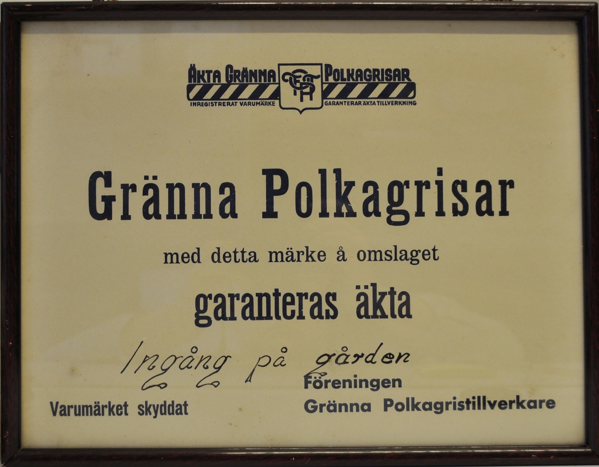 Inramad skylt med tryckt text: Äkta Gränna polkagrisar inregistrerat varumärke Garanterat äkta tillverkning Gränna Polkagrisar med detta märke å omslaget garanteras äkta
Handstriven text: ingång på gården
Tryckt text: Varumärket skyddat Föreningen Gränna Polkagristillverkare