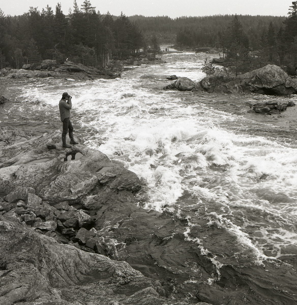 En person står på ett stenblock och fotograferar under en utflykt till Hylströmmen, 8 juni 1986.