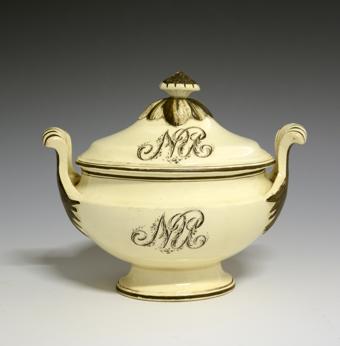 Sauseterrin med lokk og løst underfat. Høy lokknapp og høyreiste hanker i hver side. Sort dekor of sorte kantrender. MOnogrammet "NU" både på lokket og korpus.