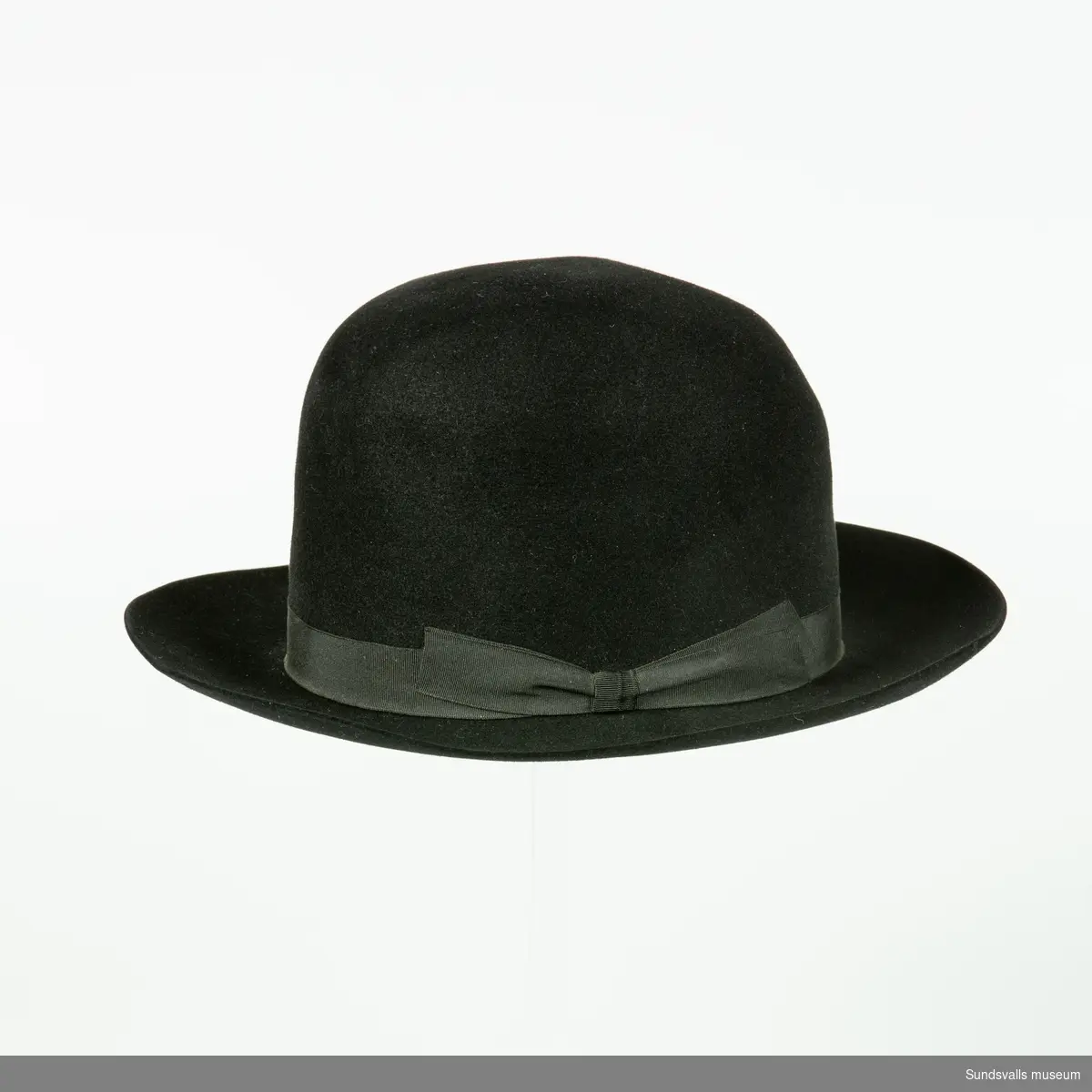 Svart herrhatt med stukad kulle och svart band. I läderbandet på insidan av hatten är 'JD' utstansat. Hatten är också märkt 'Dobesch Wien Deluxe Import'.