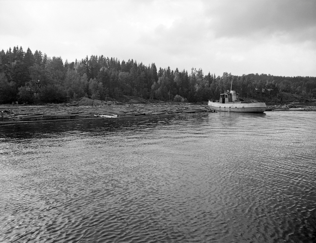 Slepebåten Vister, fotografert i arbeid med et tømmerslep ved Sleppetangen i Spydeberg kommune i Østfold.  Båten er fotografert skrått bakfra idet den dytter på slepet med baugenden.  På stranda i bakgrunnen skimtes bergnabber mot vannet og en bakkekam med skog.  Tømmerslepene ble hentet fra Fetsund lenser i nordenden av innsjøen med slepebåten Mørkfos og vanligvis fortøyd mot land, før denne båten returnerte nordover for å hente et nytt slep påfølgende dag.  Slepene besto av «moser», tømmerbunter som var bundet sammen ved hjelp av «grimer» (vaierbind) og holdt ihop ved hjelp av vaiere langsetter og på tvers av slepet, med «ringbommer» som utvendig sikring.  Ringbommene skulle hindre at enkeltstokker løsnet fra slepet og ble liggende på sjøen og drive.  Ved Sleppetangen skulle slepene befris for vaierbind, slik at stokkene kunne flyte fritt nedover den nedre delen av Glomma, gjennom tømmerrennene forbi kraftverkene ved Solbergfoss, Kykkelsrud og Vamma, hvor det ikke var plass for buntet tømmer. 