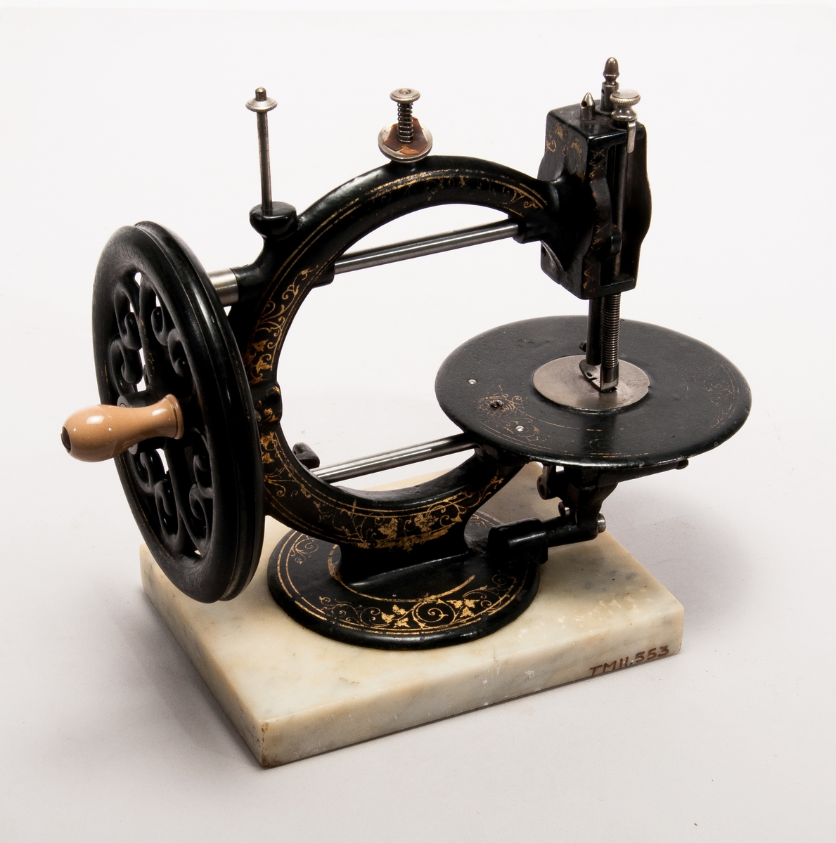 Handdriven symaskin på marmorplatta."The little Wanzer", för dubbeltrådig söm, med fram- och återgående skyttel enligt Howes patent. Märkt: R.M. Wanzer & Co. Patentees & Manufs Hamilton Canada West: Time utilizer. Trade (timglas) mark. Patented in America Gt Britain and the continent May 16 & June 17 1867".
Tillbehör: låda av trä med skjutlock och handtag, trälådans mått: 360x310x185,  Vikt:3,3kg, starkt sliten,  skyttel, 5 st spolar (2 saknas), 4 st fållvikare (saknas), 2 st ramar (?) för brodering(?), 2 st hållare (?) för brodering (?), 2 st kulor med filt (smörjkoppar ?).