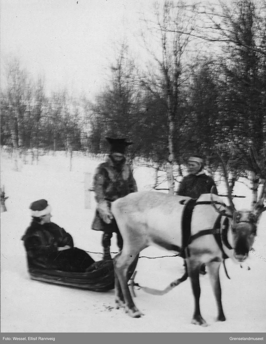 Ellisif Wessel sittende i pulk, tre samer, en kvinne og to menn, står ved siden av. Den ene mannen er sannsynligvis Ole Johnsen Must.