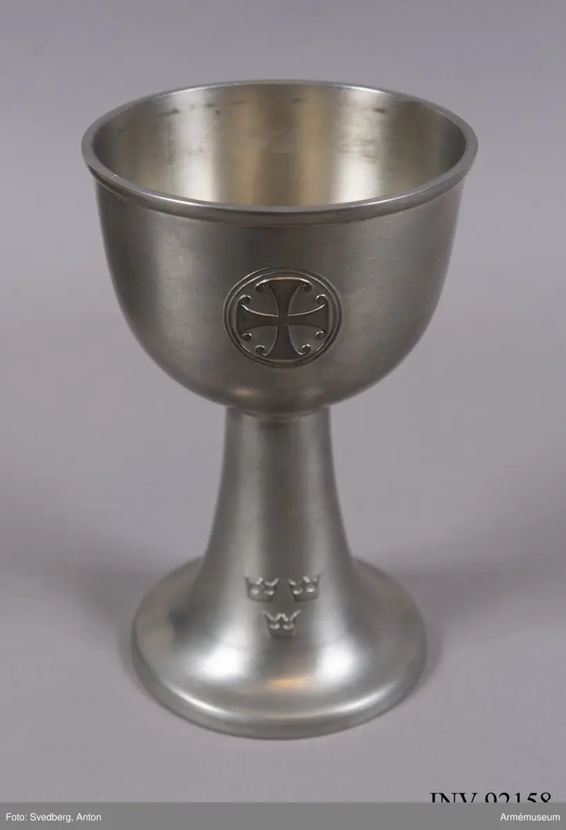 Modellexemplar av nattvardskalk m/1940, större modell i tenn. Märkt "N Redeby" inuti foten. Förvaras tillsammmans med paten i svart fodral försett med sigill samt etikett signerad av byråchefen för Kungliga arméförvaltningens intendenturdepartement den 15 april 1940.