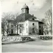 Kung Karl sn, Kungsör.
Exteriör av Kung Karls kyrka, med stenmur och träd i förgrunden, 1947.