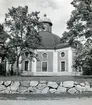 Kung Karl sn, Kungsör.
Kung Karls kyrka, exteriör med stenmur och träd framför kyrkan .