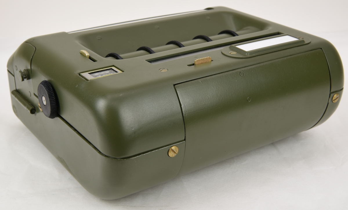 Krypteringsapparat (:1) med hölje av grönmålat aluminium i rundade former. Översidans framkant är lätt fasad och har ett avlångt fönster med alfabetet i över- och nederkant. Fönstret är till för att visa den alfabetsrulle som gav lösningen på kryptot. Under fönstret finns en svart skylt med vit text där siffrors bokstavskoder visas. På ovansidans mitt finns fem smala chifferhjul av svart bakelit i en försänkning. Hjulen är till för att ställa in chiffrets bokstäver som syns i ett fönster längst upp på apparatens ovansida. Till höger om chifferfönstret finns ett räkneverk med fyra siffror.

På apparatens framkant finns en skylt med M-nummer, serienummer och liknande och till höger ett vred av svart bakelit för att mata fram alfabetsrullen. På apparatens vänstra sida finns ett frammatningsvred av metall samt tillverkarens logotyp. På den högra sidan finns en lucka för alfabetsrullen och ett vred av bakelit för att ställa in chifferhjulaxeln. Baksidan har en större lucka för hålkortsplatsen och undersidan har små gummifötter samt en dekal med information om garantitid.

Till apparaten hör också en transportväska (:2) av formgjuten och genomfärgad gummi. Väskan är grön och har en vävd bärrem fäst med mässingsskruv. Locket är fäst med ett avlångt, nitat gångjärn och har ett låsspänne i mässing. På locket finns tre kronor och apparatens M-nummer i relief och på väskans undersida finns väskans M-nummer. Insidan av väskan är formad efter kryptoapparaten för att ge så mycket skydd som möjligt.

M-nummer: M 3858-301010
Tillverkningsnummer: 22749

Väskans M-nummer: M 7038-045010