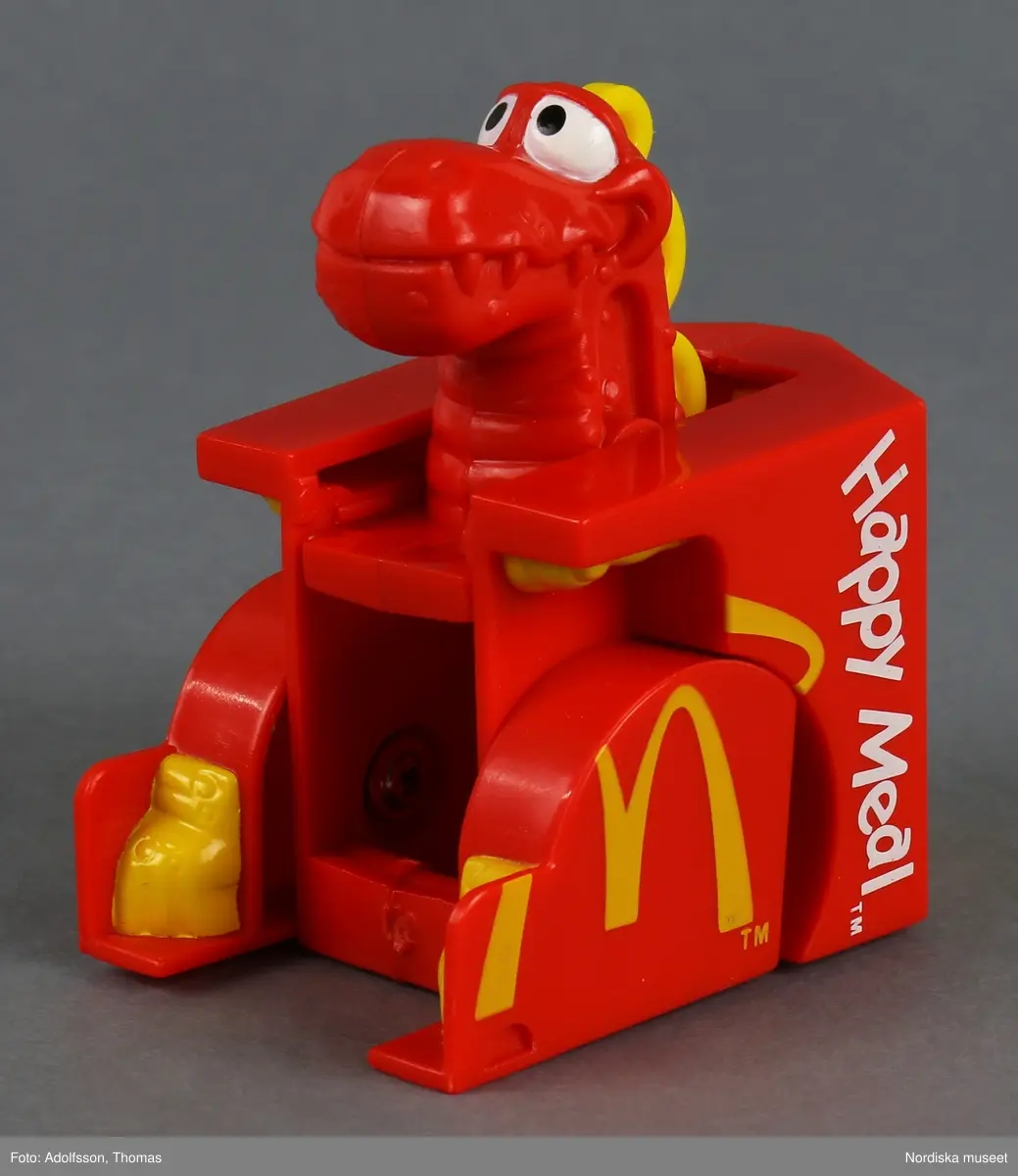 Leksak i form av en röd matkartong för hamburgare. På utsidan finns texten "Happy Meal" och symbolen M som står för matkedjan McDonald's. Sidorna går att fälla ut, varvid en djurfigur med huvud och tassar framträder.