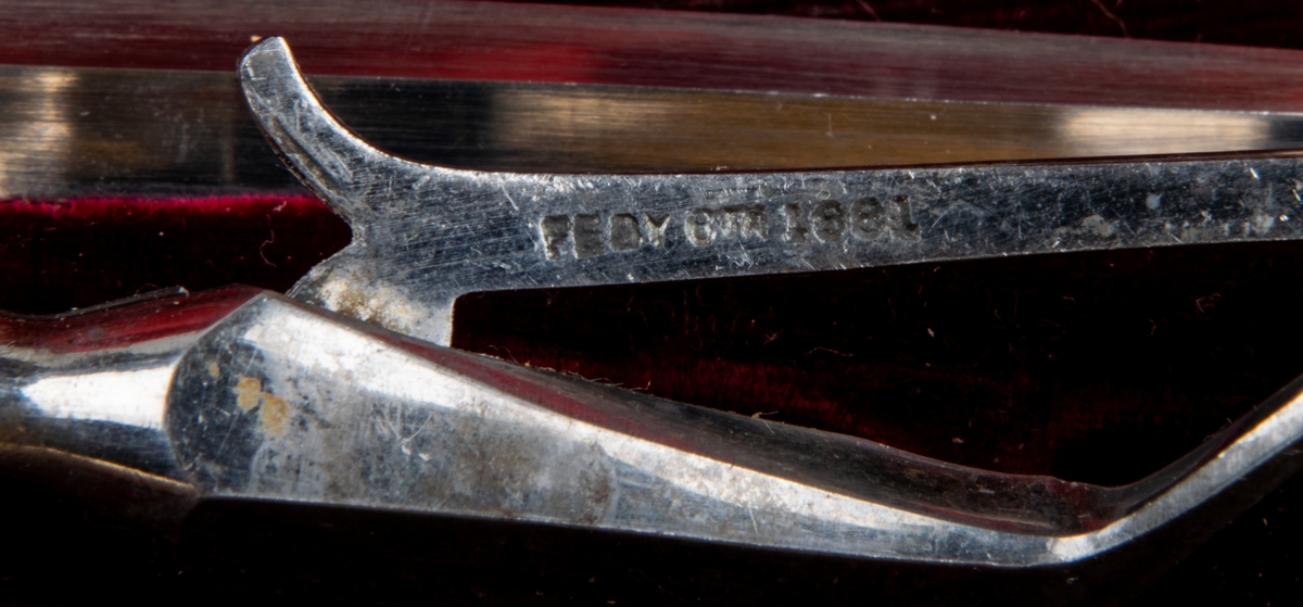 Stekgarnityr i svart fodral med initialerna P.E. i guld. Skaft med snirkligt monogram. Stämpel "V R".

Harrison Bros & Hovsson Cutlers to her Majesty.