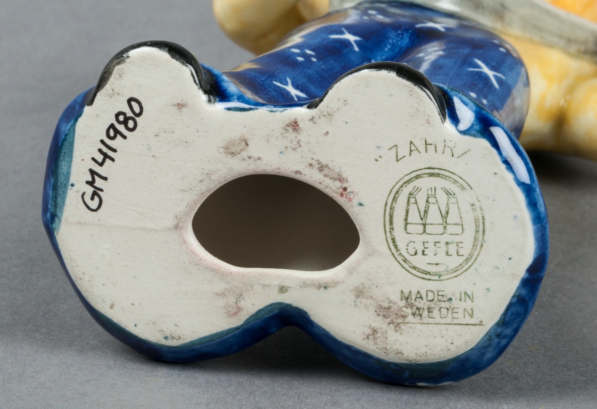 Figurin Zahra, kvinna spelande mandolin, glaserad i främst gult och blått. Tillverkad av Gefle Porslinsfabrik, formgiven av Märta Willborg 1937.