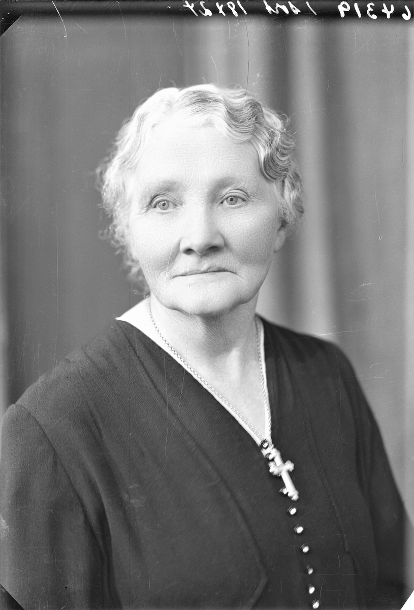 Portrett. To foto med lyshåret eldre kvinne i mørk kjole med perleknapper i front. Kors om halsen. Gruppebilde. Familiegruppe på fire. Fire foto med ung lyshåret mann i mørk stripet dress, mørk vest, hvit skjorte og mørkt slips, ung mørkblond kvinne i mørk mønstret kjole med hvite striper og hvite knapper i front, ung mørkblond kvinne i mørk kjole med broderinger i front og hvt krage. Lyshåret eldre kvinne i mørk kjole med perleknapper i front. Kors om halsen. Bestilt av Fru Serine Dybdal Henriksen.