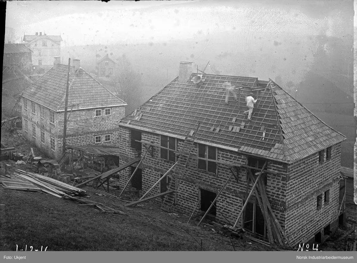 Femrader'n under bygging. Taktekking av hus. Menn arbeider på taket med takstein.