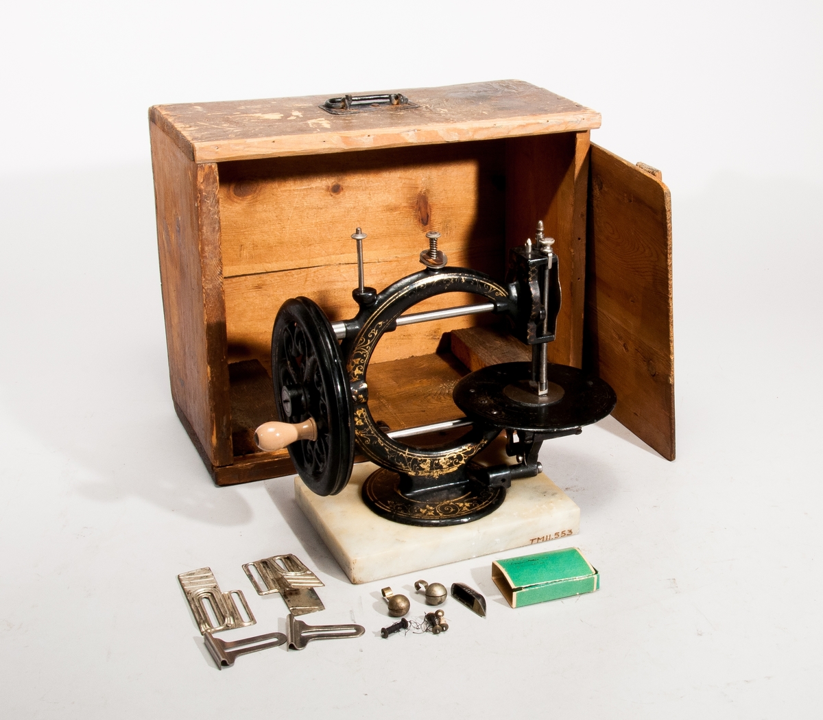 Handdriven symaskin på marmorplatta."The little Wanzer", för dubbeltrådig söm, med fram- och återgående skyttel enligt Howes patent. Märkt: R.M. Wanzer & Co. Patentees & Manufs Hamilton Canada West: Time utilizer. Trade (timglas) mark. Patented in America Gt Britain and the continent May 16 & June 17 1867".
Tillbehör: låda av trä med skjutlock och handtag, trälådans mått: 360x310x185,  Vikt:3,3kg, starkt sliten,  skyttel, 5 st spolar (2 saknas), 4 st fållvikare (saknas), 2 st ramar (?) för brodering(?), 2 st hållare (?) för brodering (?), 2 st kulor med filt (smörjkoppar ?).