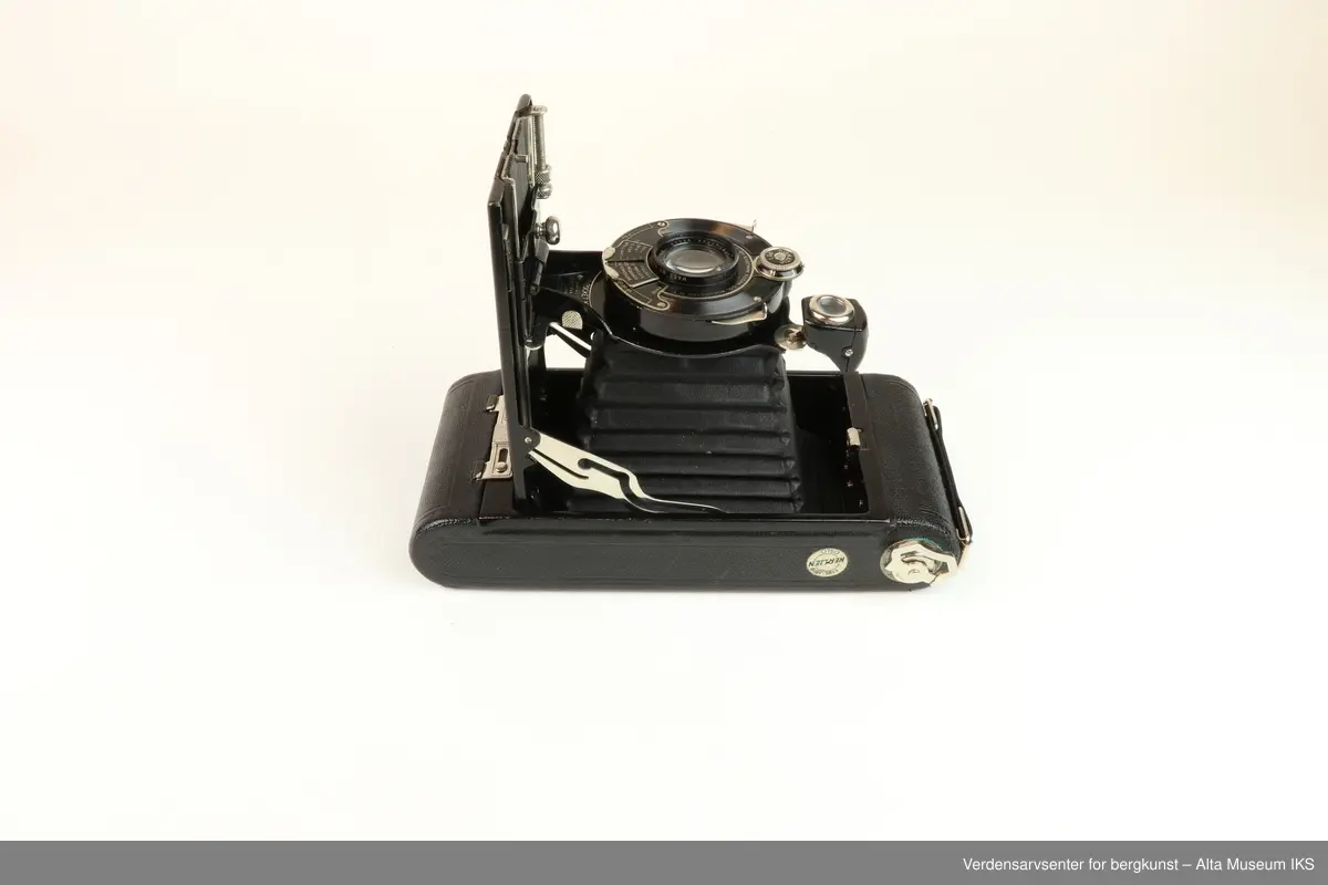 Foldet fotoapparat Diomatic NO. 1A Pocket Kodak. Made in U.S.A by Eastman Kodak Company. Rochester. N.Y.
Kodak Anastigmat F 6.3-12.7mm lens NO. 18339.
Kamera med rektangulær form og avrundede sider. 
På undersiden et hull med gjenger der noe kan skrus inn.
På oversiden metalldel med en nøkkellignende utsikker som kan vris rundt.
Metallås. Firkantet luke på baksiden for kameralinsen, og rundt rødt vindu til bildetelling.
Åpnes ved å dra ned metallås.
Kameraet kommer i et brunt lærveske med 530mm lang stropp.