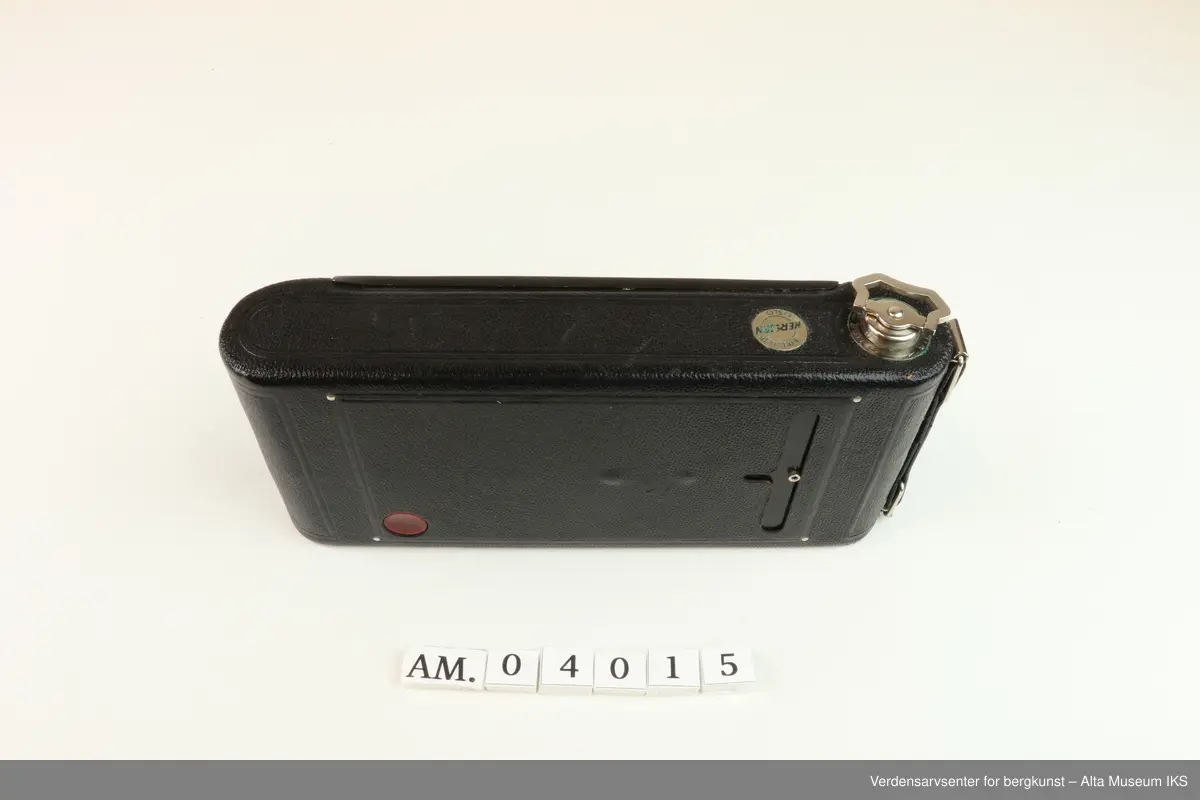 Foldet fotoapparat Diomatic NO. 1A Pocket Kodak. Made in U.S.A by Eastman Kodak Company. Rochester. N.Y.
Kodak Anastigmat F 6.3-12.7mm lens NO. 18339.
Kamera med rektangulær form og avrundede sider. 
På undersiden et hull med gjenger der noe kan skrus inn.
På oversiden metalldel med en nøkkellignende utsikker som kan vris rundt.
Metallås. Firkantet luke på baksiden for kameralinsen, og rundt rødt vindu til bildetelling.
Åpnes ved å dra ned metallås.
Kameraet kommer i et brunt lærveske med 530mm lang stropp.