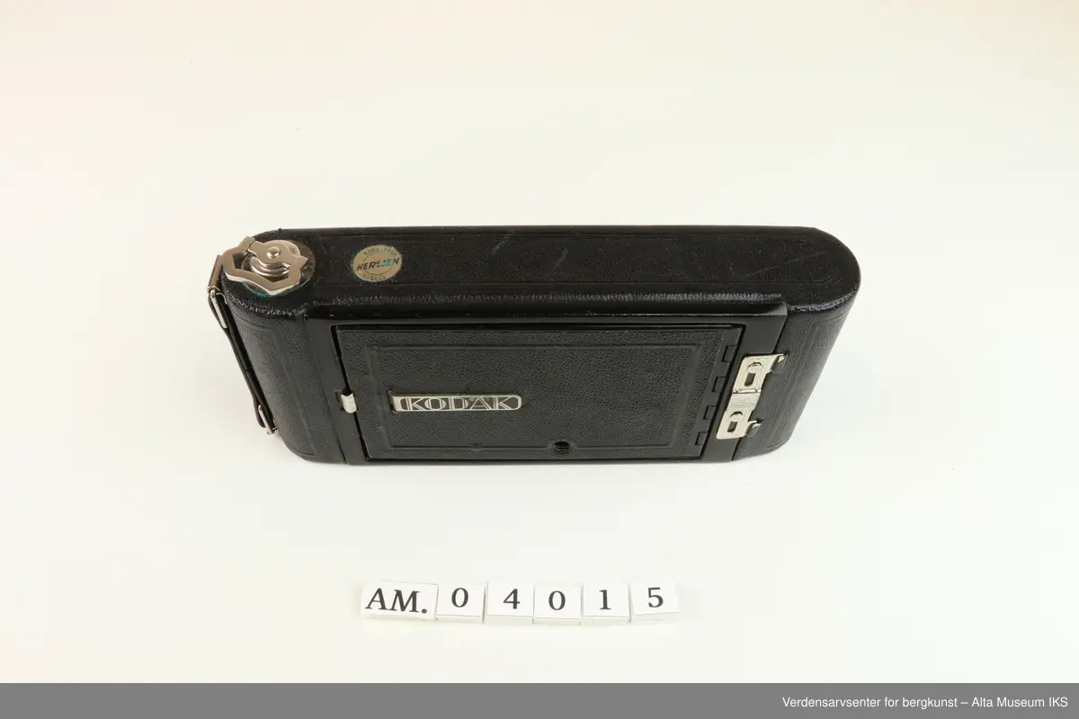 Foldet fotoapparat Diomatic NO. 1A Pocket Kodak. Made in U.S.A by Eastman Kodak Company. Rochester. N.Y.
Kodak Anastigmat F 6.3-12.7mm lens NO. 18339.
Kamera med rektangulær form og avrundede sider. 
På undersiden et hull med gjenger der noe kan skrus inn.
På oversiden metalldel med en nøkkellignende utsikker som kan vris rundt.
Metallås. Firkantet luke på baksiden for kameralinsen, og rundt rødt vindu til bildetelling.
Åpnes ved å dra ned metallås.
Kameraet kommer i et brunt lærveske med 530mm lang stropp.