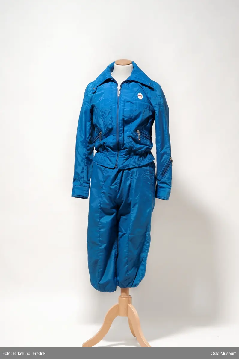 Dameskidress i tre deler. A: Kort jakke og B: Bukse med vide ben og seler. Begge deler i blått boblestoff av polypropylen i størrelse 42. C: Vest i kremhvit farge i samme stoff og størrelse.