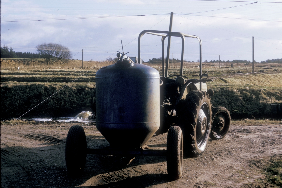 Forsøgsdambruget i Brøns, Danmark, 1974 : Traktor med tankvogn. Vogna holder fiskefôr som fordeles ut i dammene med fisk.