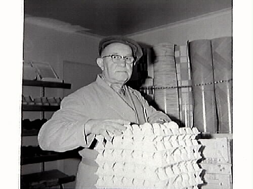 John Johansson står vid en trave ägg i Konsum Frillesås. I bakgrunden står rullar med vad som kan vara prover på olika linoleummattor.
Bild 2 visar John med en i papp inslagen sockerpaket på axeln.