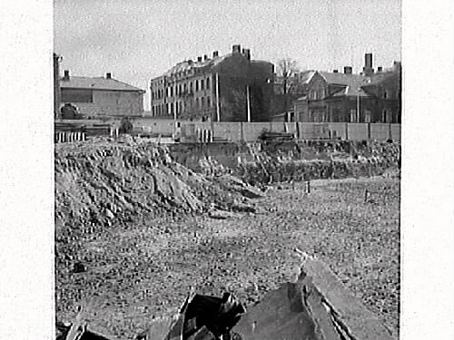 Fastigheten kv Trädgården 6, Varberg. Grundschaktning för Domusbygget är klart. Artikel i samband med bilden publicerad i Varbergs Tidning 1962-05-07.
Fotot visar den urschaktade marken och omgivningarna. Fastigheterna i bakgrunden är Läkaren 9, (Varbergs stadshotell), Rappeska huset (revs 1969?) och en del av Brunnsparken 5.