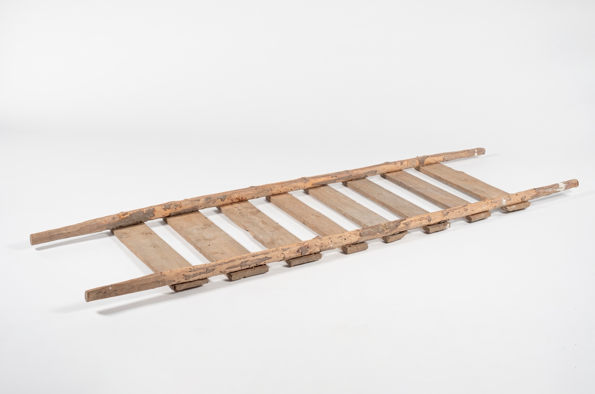 Rektangulær båre, brukt til å bære slaktegris. Består av 8 planker lagt på tvers og spikret fast til to trestenger. Det er rester av bark på stengene, og endene som er håndtak er spikket til for bedre grep.