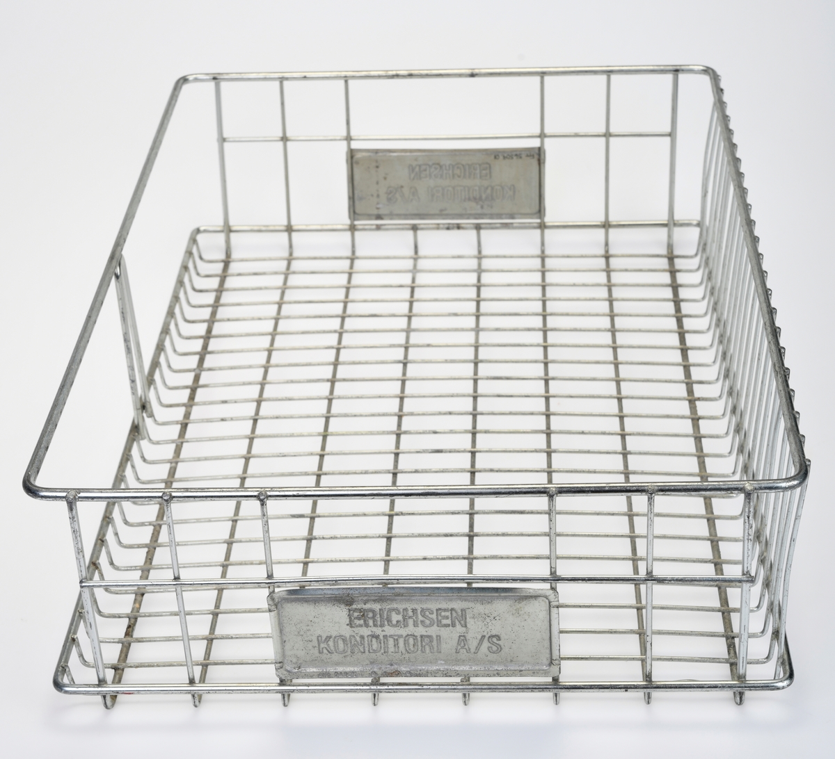 To identiske trådkurver av metall. Kurvene er firkantet med avrundede hjørner. I bunnne er rutene 2,5x5,0cm og i bakkant er de 2,5x13,0cm. På kortsidene er det ruter på sidene og et håndtak på midten. Under håndtakene er det montert på metallskilt med tekst, se "Påført tekst/merker". I front er kurvene åpne med unntak av en bøyle på midten. Kurvene er brukt på Konditor Erichsen, trolig til transport av bakst.