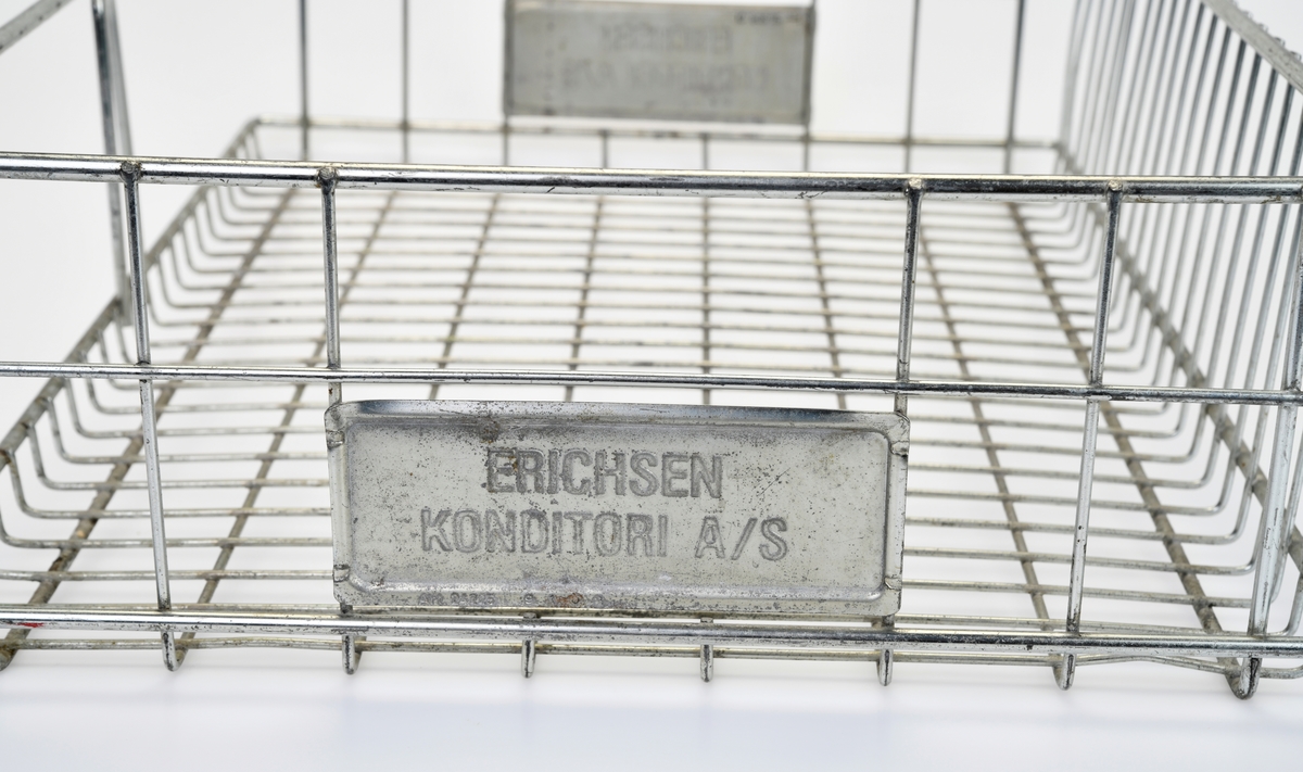 To identiske trådkurver av metall. Kurvene er firkantet med avrundede hjørner. I bunnne er rutene 2,5x5,0cm og i bakkant er de 2,5x13,0cm. På kortsidene er det ruter på sidene og et håndtak på midten. Under håndtakene er det montert på metallskilt med tekst, se "Påført tekst/merker". I front er kurvene åpne med unntak av en bøyle på midten. Kurvene er brukt på Konditor Erichsen, trolig til transport av bakst.