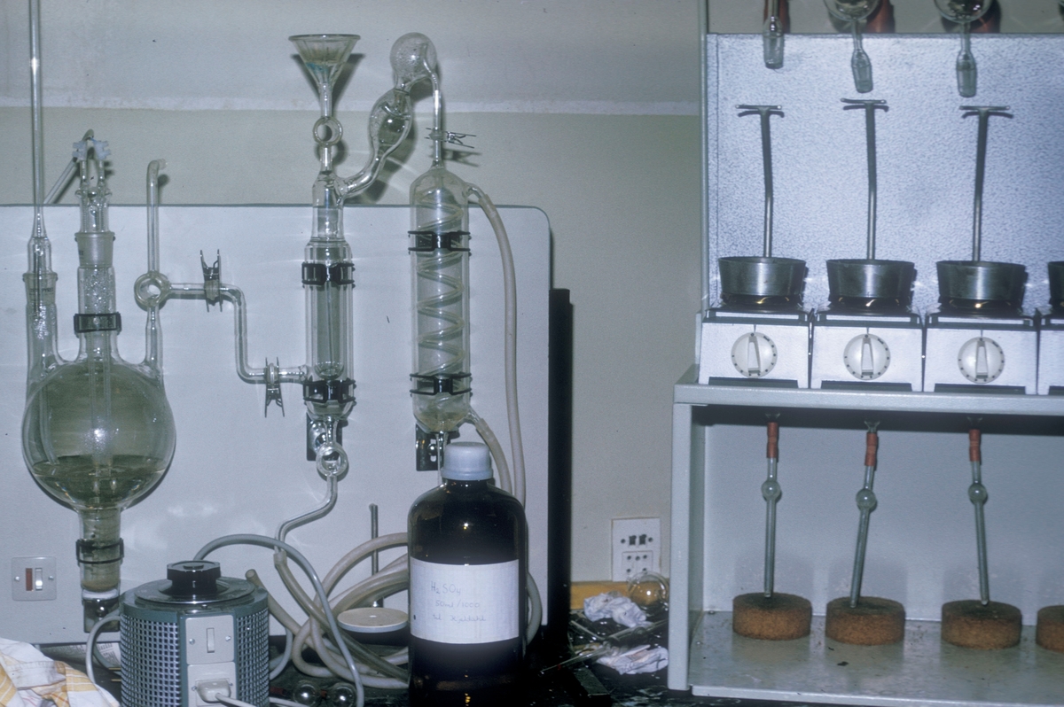 Forsøgsdambruget i Brøns, Danmark, 1974 : Laboratorium med diverse apparater, glass og instrumenter på en arbeidsbenk.