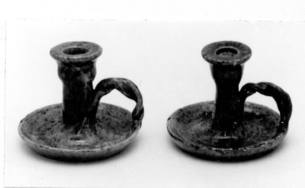 Handdrejad ljusstake av lergods, typ kontorsljusstake. Ljushållare för ett ljus på rund fotplatta med vriden grepe. Ljusgrön bottenlasyr med gröna och bruna sänk. Fotplattan är sprucken tvärs över. På undersidan oläslig text.