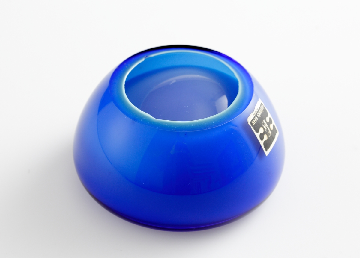 Blå skål i en rund och mjuk design. 
Etikett: Vit med ett stort svart dubbel-E med texten "Elme" och "Hjördis Une" i vitt.