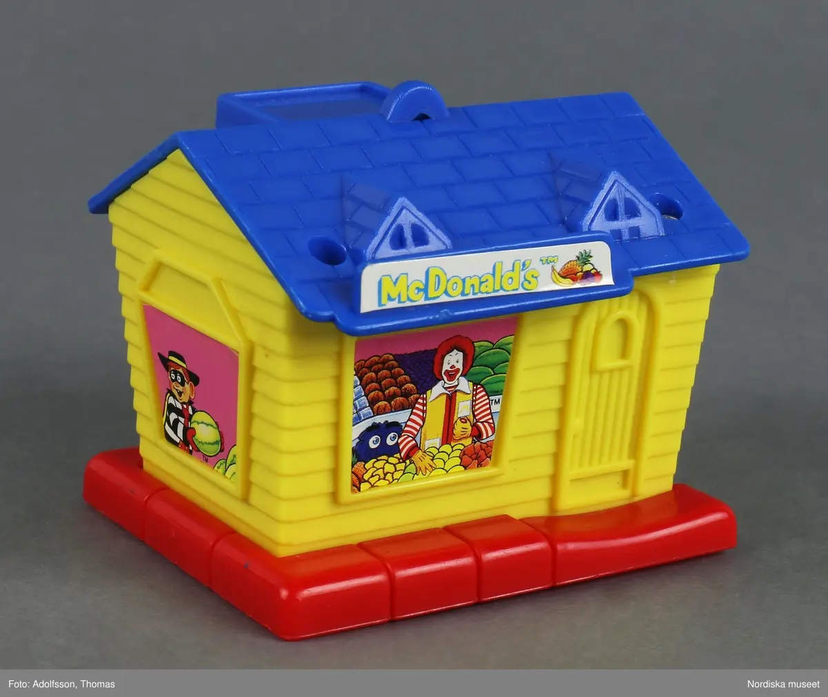 Leksakshus som föreställer en fruktaffär i miniatyr. Huset har flera fönster, dörr och skorsten. En clown, en maskerad pojke och ett lila spöke, tre figurer som ofta förekommer i McDonald's reklam, finns avbildade medan de plockar frukt. På taket finns en skylt med företagets namn och en hög med frukt. Metallskruvar håller ihop delarna.