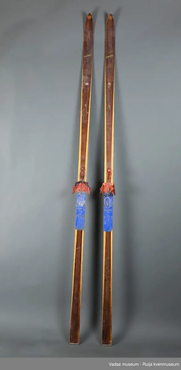 Langrennski av tre. Skiene er lakkert i brunt og klarlakk over og under, i vekselvise felter i skiens lengderetning. Bindinger av tåbindings-typen i aluminium; rød binding og blå hælplate. Avrundet renne langs skiens glideflate. Rett avskåret baktupp med metallbeslag. På skiens overside er flere emblemer. På tuppen er et rundt emblem med bilde av en bagler og påskriften "Splitkein Østbye Patent". Lenger ned på skien er et Gresvig-sport emblem. Videre ned mot bindingen er et rundt emblem av en bagler mot rød bakgrunn.