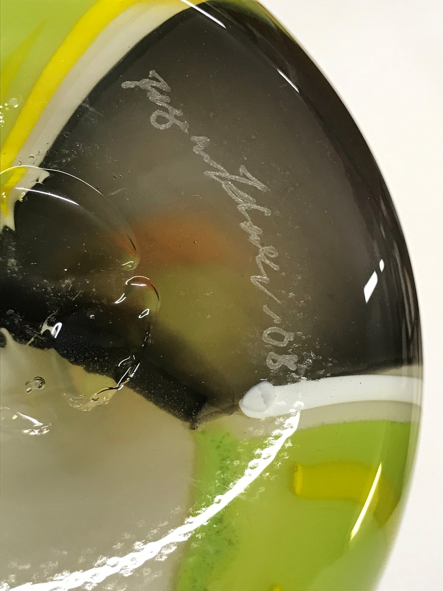 Mosaikmönstrad urna med lock. Mosaiken är tillverkad genom att konstnären först tilverkar planglas i olika färger, vilka sågas upp i småbitar som läggs i ett mosaikmönster. Dessa välsas in i en post av ofärgat glas. Över detta anfångas mer ofärgat glas som formas till önskat föremål.