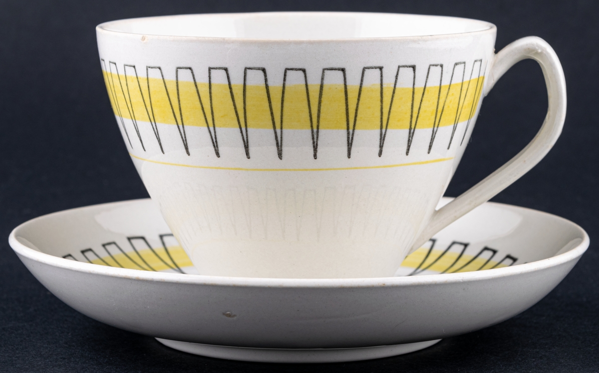 Kaffekopp med fat, modell BT i dekoren Palace, form och dekor av Berit Ternell. Svart stämpeldekor med gult band.