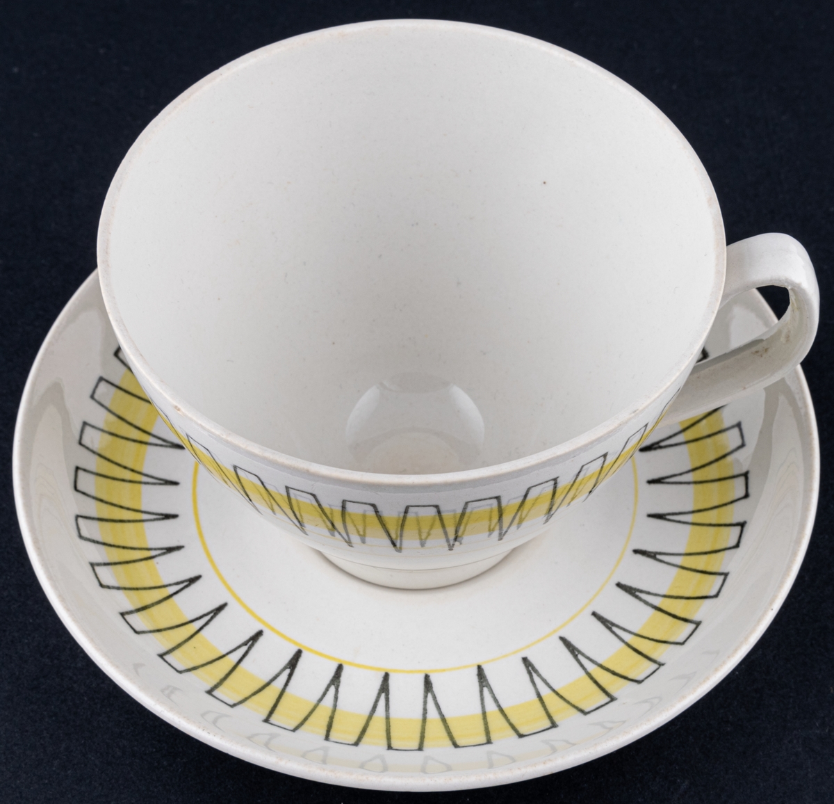 Kaffekopp med fat, modell BT i dekoren Palace, form och dekor av Berit Ternell. Svart stämpeldekor med gult band.