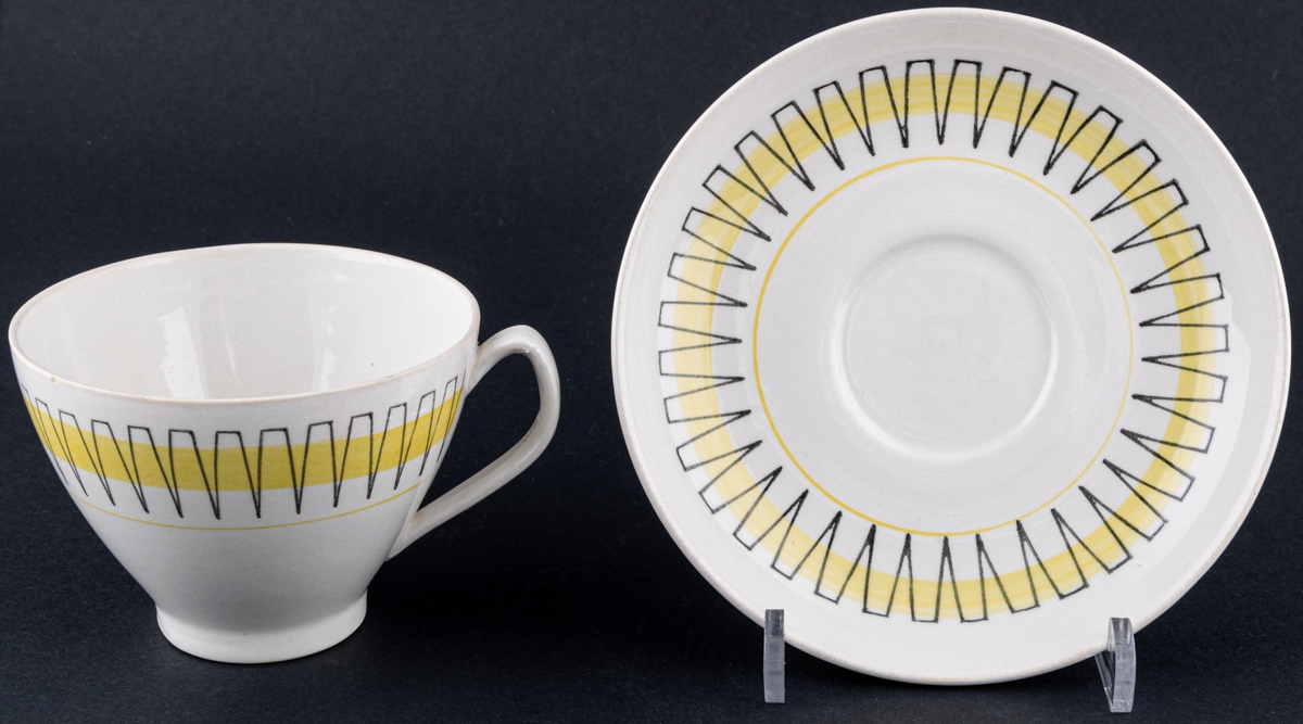 Kaffekopp med fat, modell BT i dekoren Palace, form och dekor av Berit Ternell. Svart stämpeldekor med gult band.