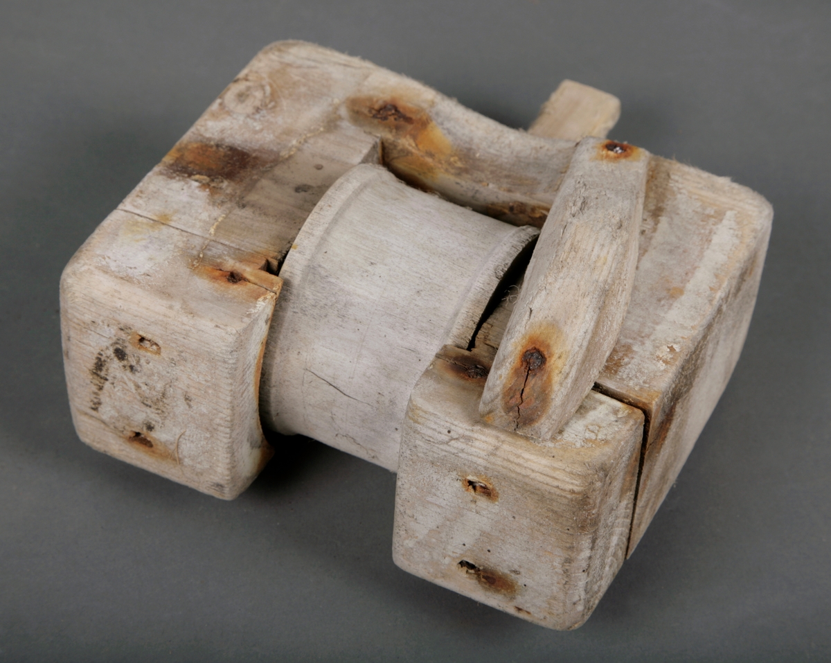 En firkantet tregjenstand med en trommel i midten som går rundt. Satt sammen med spiker.