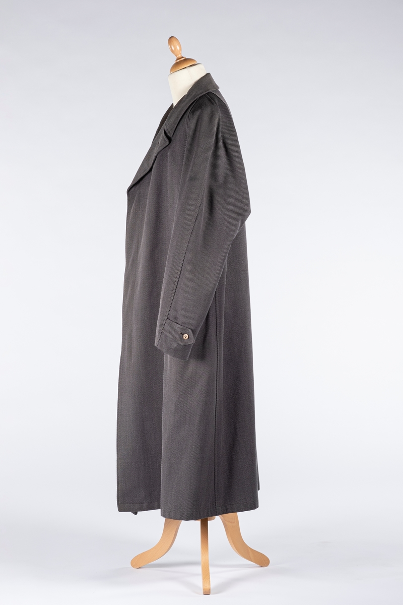 Rett frakk med slag og raglanerme. Foring av silke. Skjult knepping med fire knapper, kan også kneppe slaget under kragen. To lommer med klaff og to innerlommer. Splitt bak med knepping. Spensel nederst på ermene.