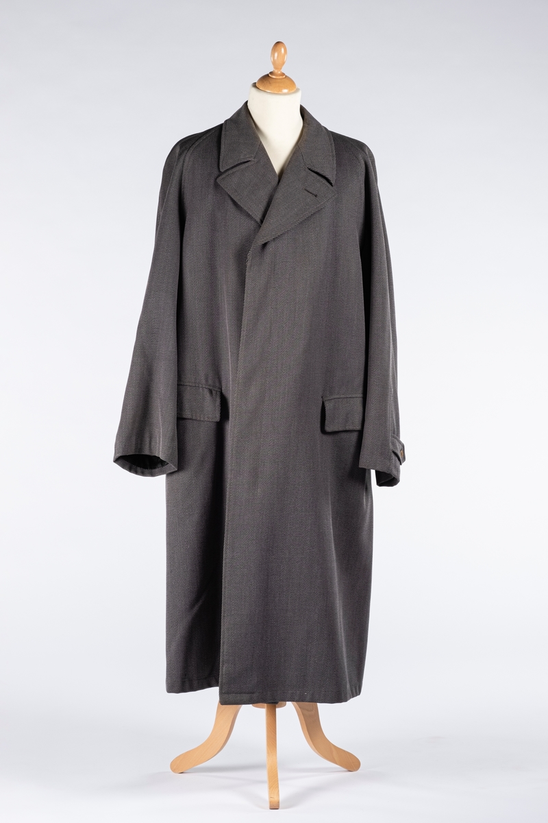 Rett frakk med slag og raglanerme. Foring av silke. Skjult knepping med fire knapper, kan også kneppe slaget under kragen. To lommer med klaff og to innerlommer. Splitt bak med knepping. Spensel nederst på ermene.