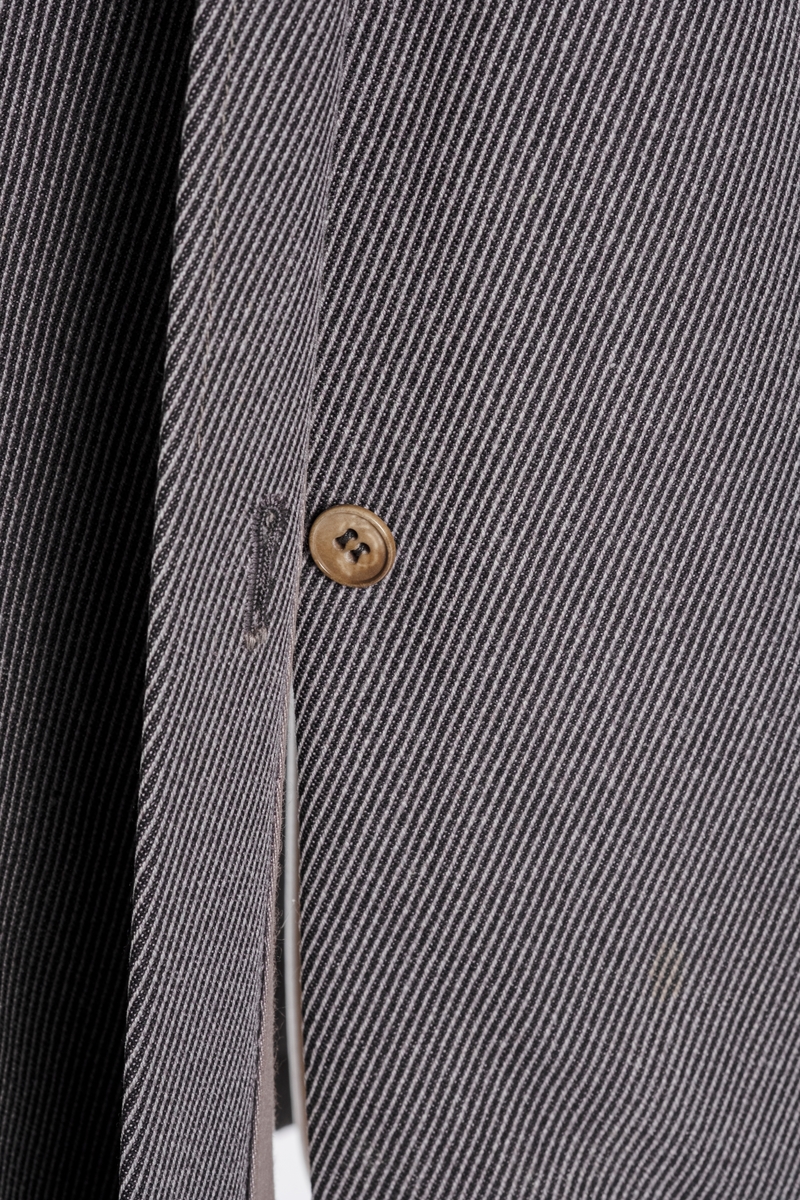 Rett frakk med slag og raglanerme. Foring av silke. Skjult knepping med fire knapper, kan også kneppe slaget under kragen. To lommer med klaff og to innerlommer. Splitt bak med knepping. Spensel nederst på ermene.